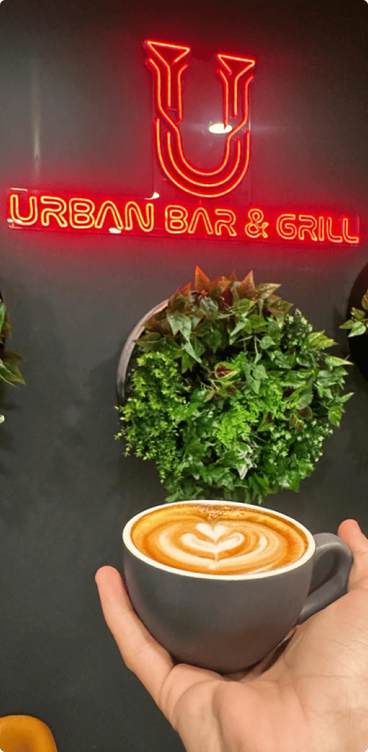 Skillfully crafted coffee art featuring a heart motif, complemented by the elegant glow of a neon sign bearing the Urban Bar Grill